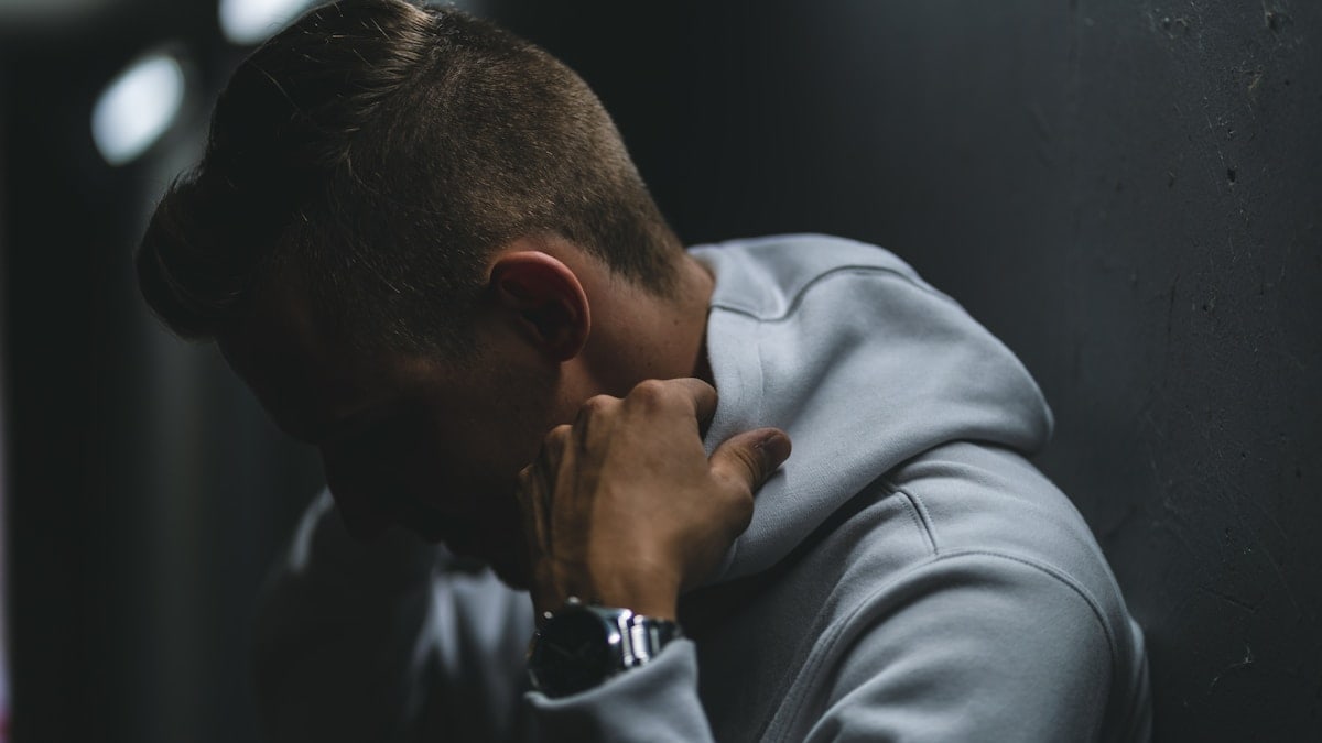 A guy standing in a dark place with a white hoodie on.